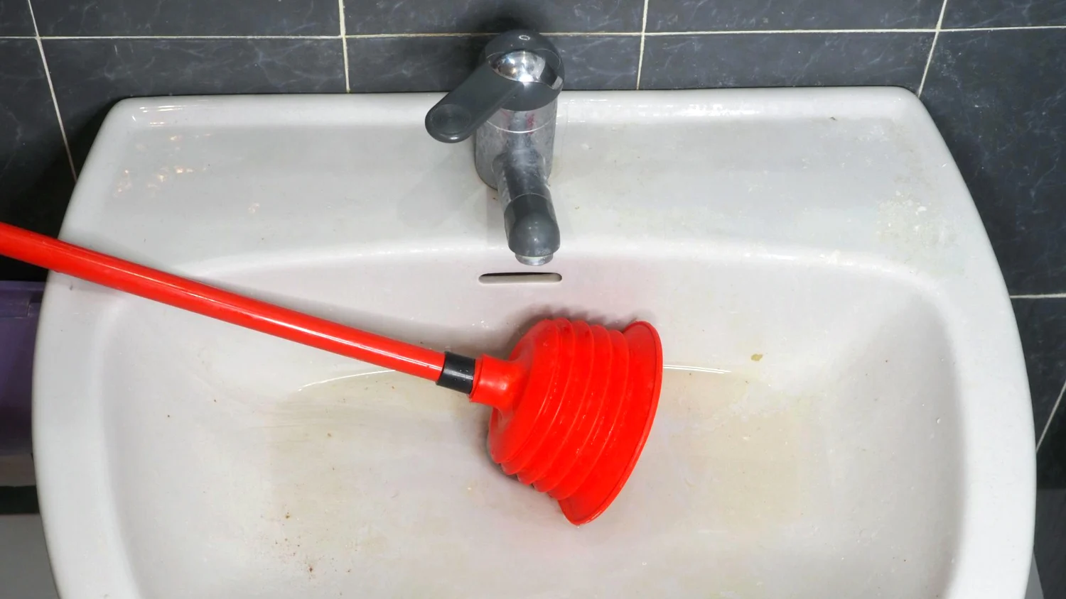 a clogged bathroom sink with a red pump